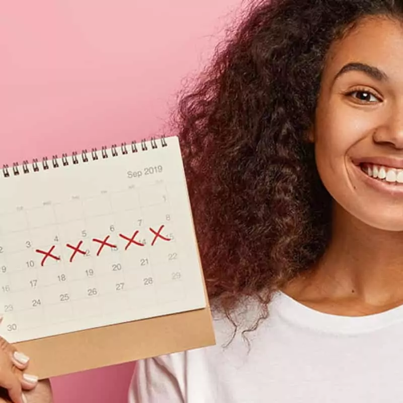 Young woman holding up simple calendar, 3 ways to delay your period image header